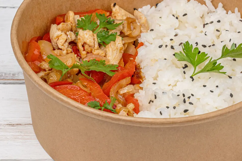 A savory chicken and rice bowl with vibrant peppers and herbs in a takeaway container.