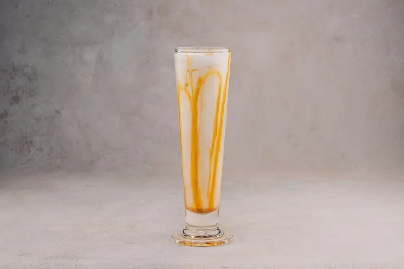 High-angle shot of a creamy caramel milkshake in a tall glass against a gray backdrop.