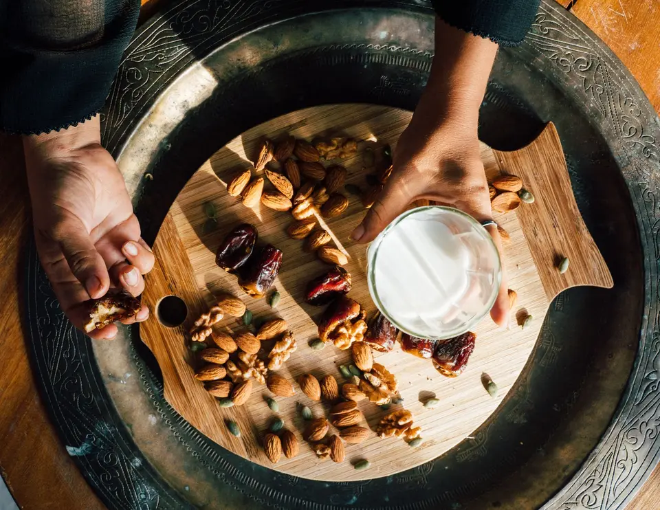 Top view of a nut and date platter with a glass of milk being held.